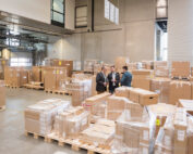 Three men in factory warehouse surrounded by cardboard boxes