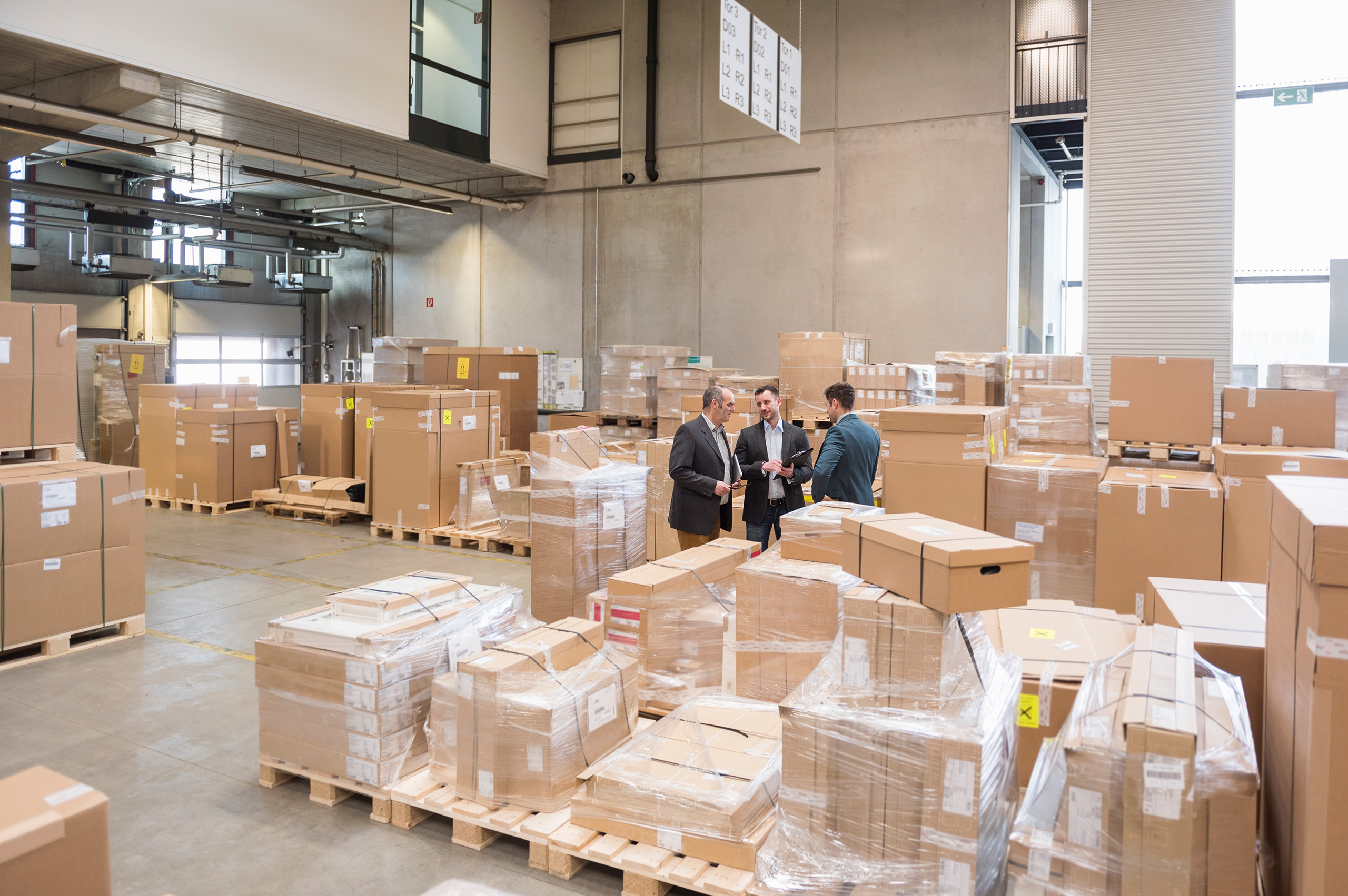 Three men in factory warehouse surrounded by cardboard boxes