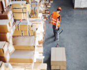 Young male worker in uniform is in the warehouse pushing pallet truck.